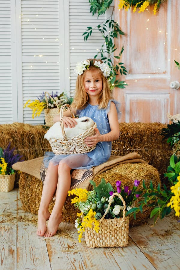 Easter composition. A little blonde girl plays and communicates with a white rabbit sitting in a basket in her arms. Child and animals. Easter composition. A little blonde girl plays and communicates with a white rabbit sitting in a basket in her arms. Child and animals.