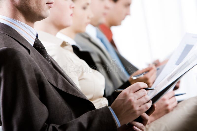 Businessman making notes during convention with row of people at background. Businessman making notes during convention with row of people at background