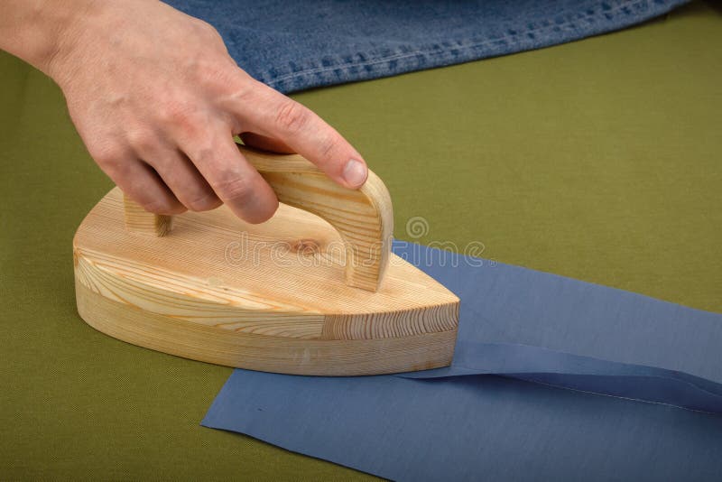 Tailor's hand smoothes the seams on the sewn product with a wooden blank for wet-heat treatment on the table. Tailor's hand smoothes the seams on the sewn product with a wooden blank for wet-heat treatment on the table