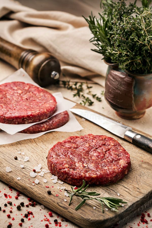Op een houten scherpe raad op kraftpapier-document zijn er ruwe rundvleesburgers voor burgers, kruiden, rozemarijn, een pepermole stock fotografie Op een houten scherpe raad op kraftpapier-document zijn er ruwe rundvleesburgers voor burgers, kruiden, rozemarijn, een pepermole stock fotografie
