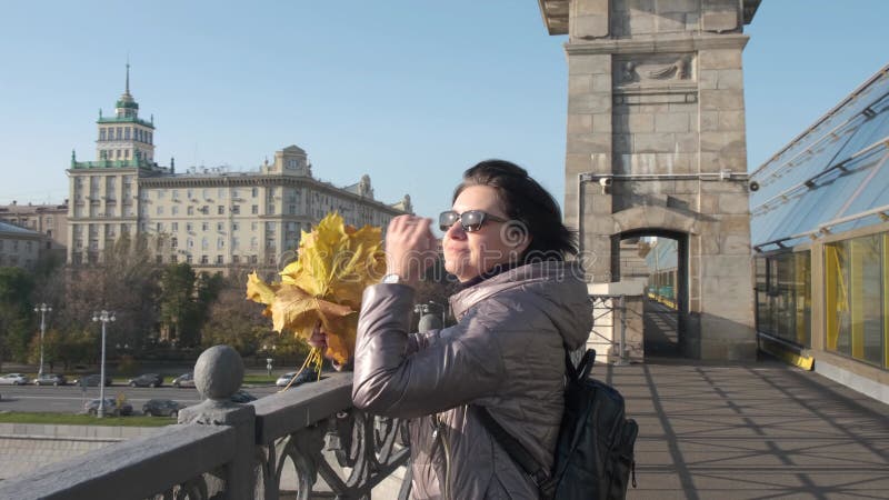 Op een zonnige herfstdag staat een vrouw van middelbare leeftijd met een boeket met gele bladeren op een brug over een rivier ..