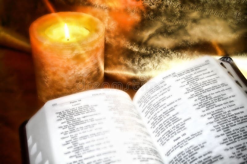 An open bible on golden foil paper with a lit amber candle. High contrast effects with a soft focus add to the ambiance.