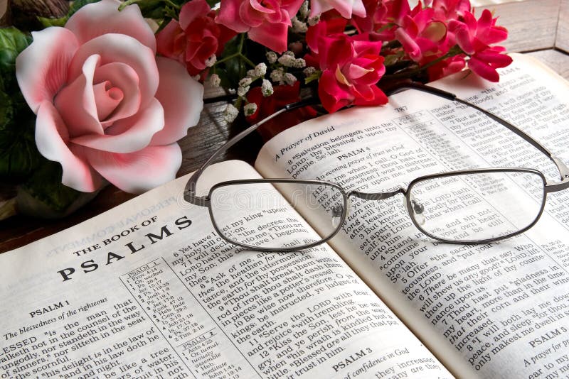 An open Bible with reading glasses lying on it and flowers in the background. An open Bible with reading glasses lying on it and flowers in the background.