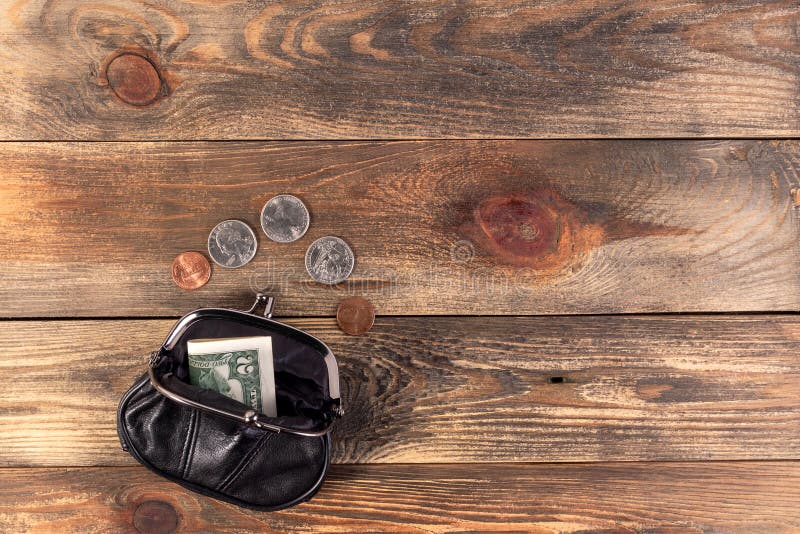 Open black leather pocket wallet with coins one cent, quarter dollar and 2 dollars banknote nearby. Financial crisis, poverty, lack money. On wooden background or table. Flat lay. Top view. Close-up