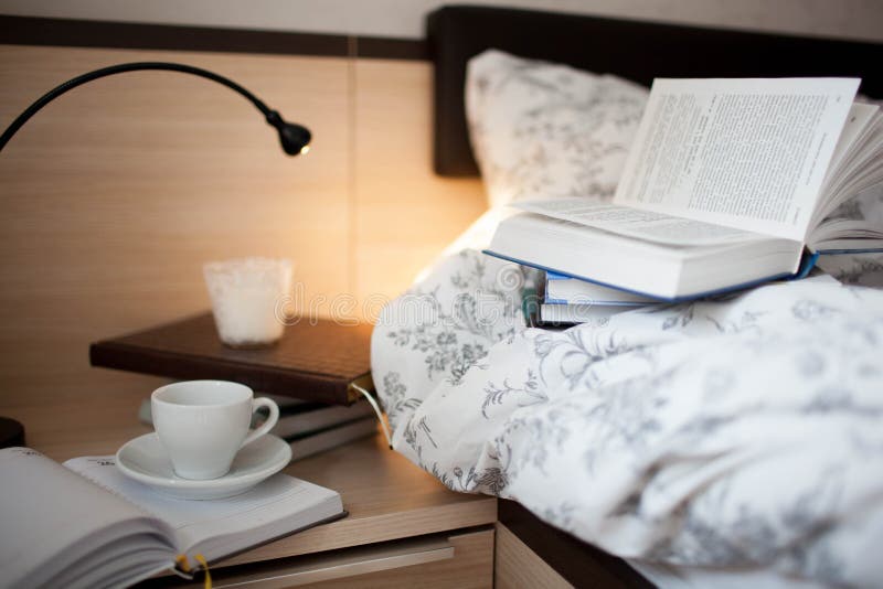 An Open Book on the Bed. Books and Coffee Cup on the Nightstand Stock