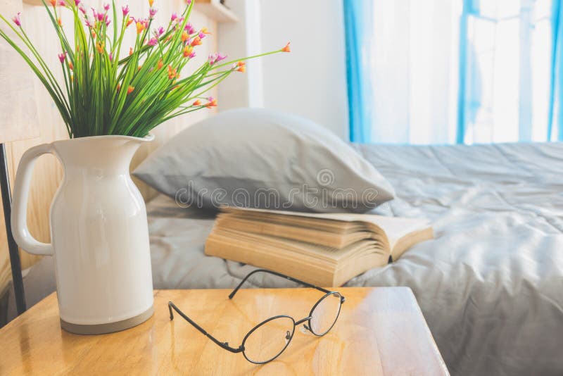 Open book on bed with flower in jug and eye glasses foreground