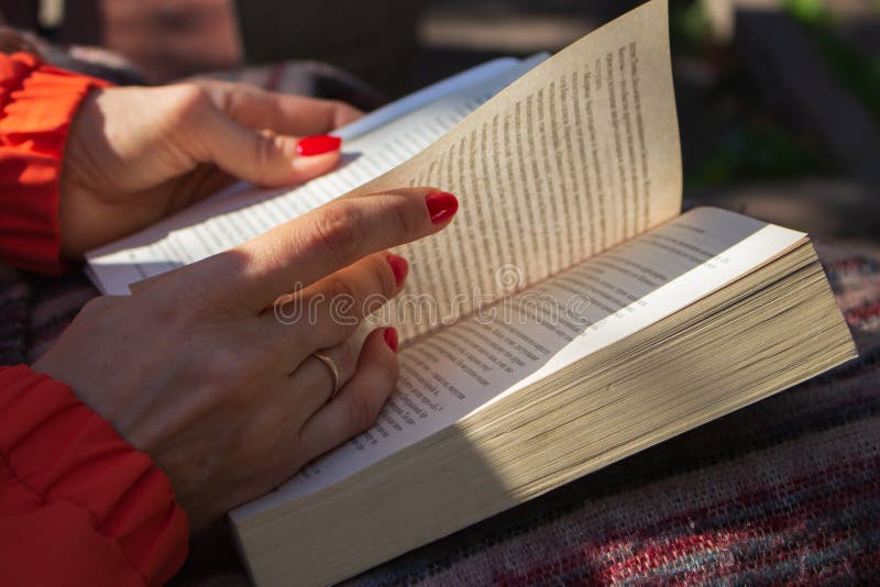 Open book in woman hands. Girl with bright nails reading book in park. Outdoor relaxation. Reading hobby. Read book on sunny day.