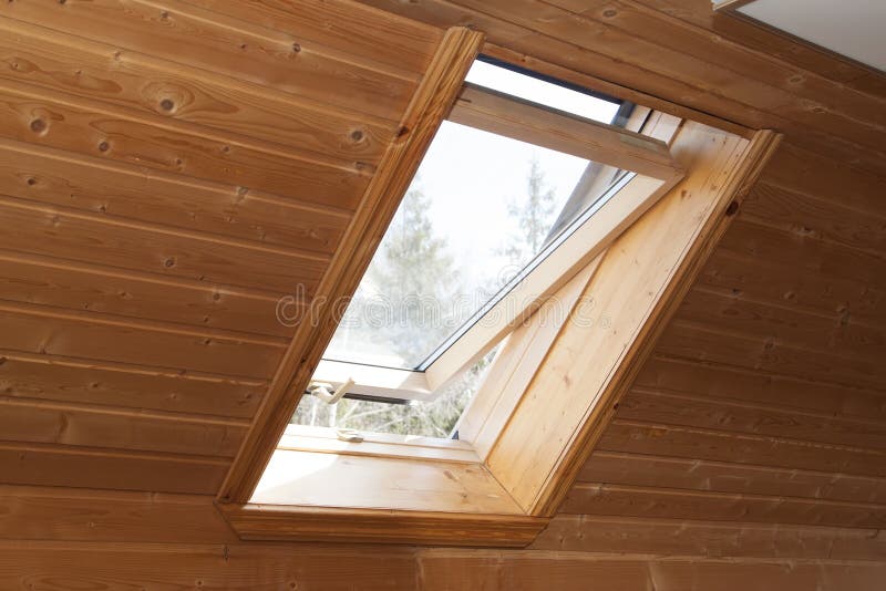 Open dormer window in wooden house in the attic. Room has sloping ceiling made of natural eco-materials and views of park through