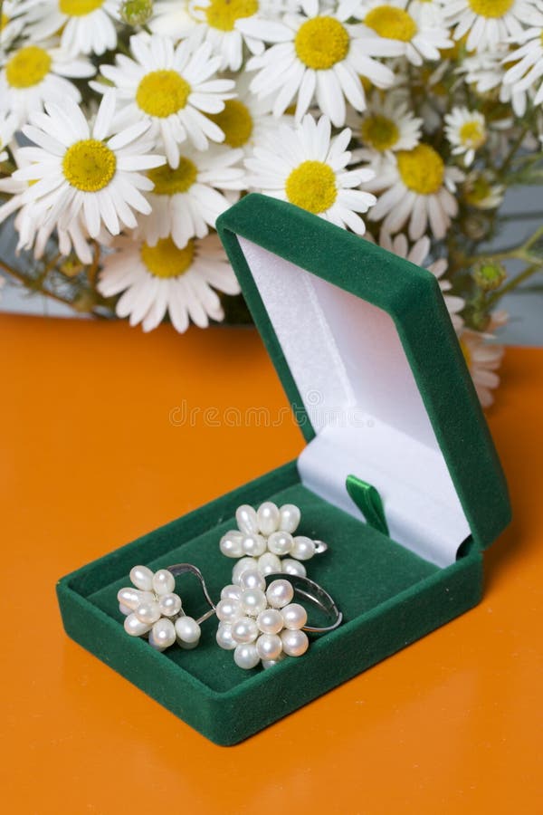 An open green velvet box for jewelry. In it lies a set: a ring and earrings with pearls. Next to the vase is a bouquet of chamomil