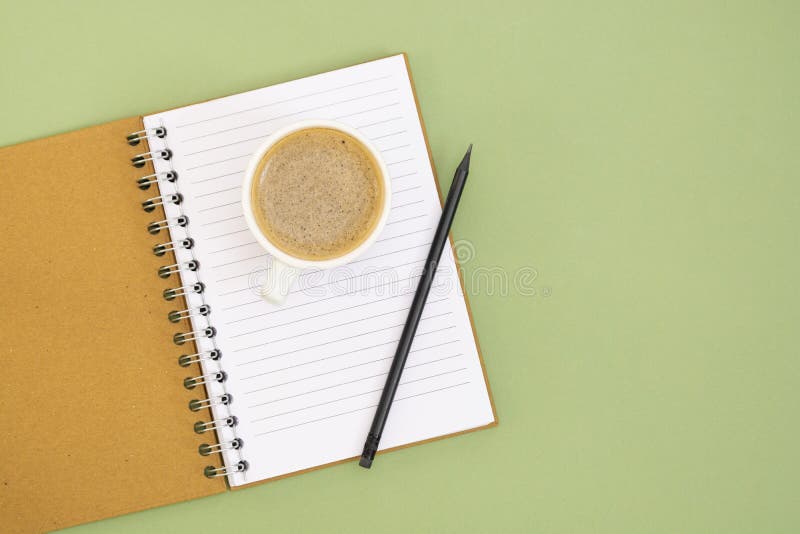 Open notebook with empty page and coffee cup. Table top, work space on green background. Minimalistic flat lay