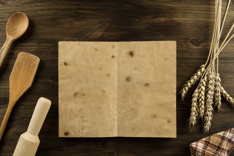 Open old vintage book on the aged wooden background. kitchen utensils, wheat, cloth.