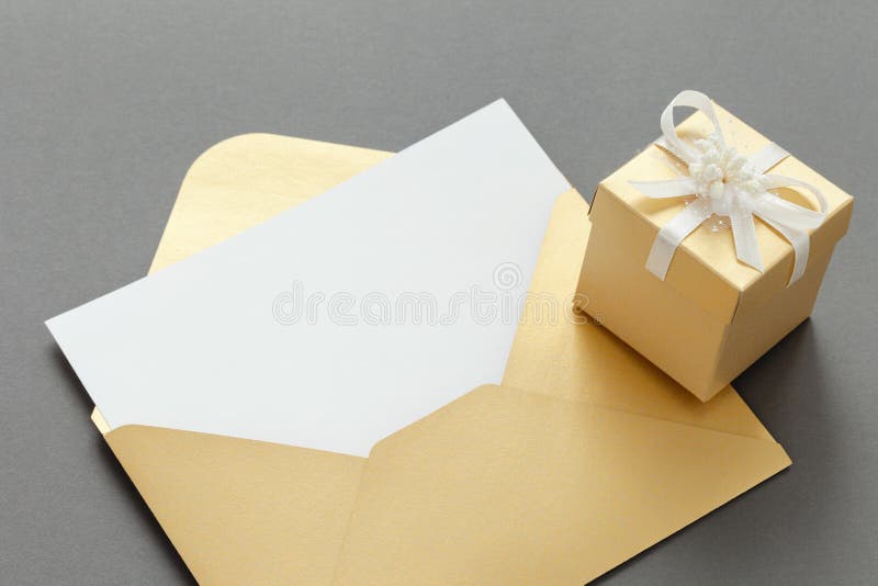 Open paper envelope golden color with blank paper sheet and gift box with ribbon on gray background.