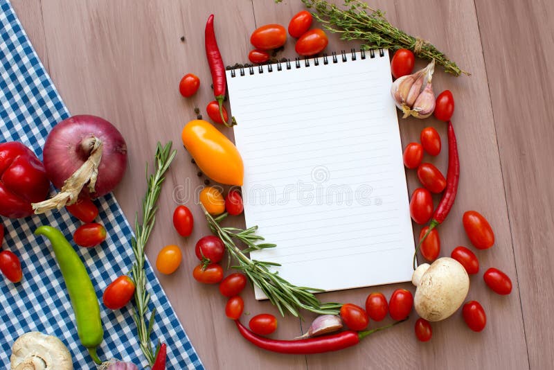 Open recipe book with fresh vegetables and herbs on wooden.