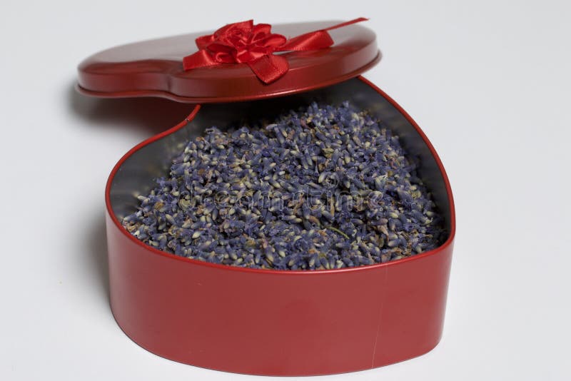 An open red box in the shape of a heart with dried lavender flowers. It stands on a white background.