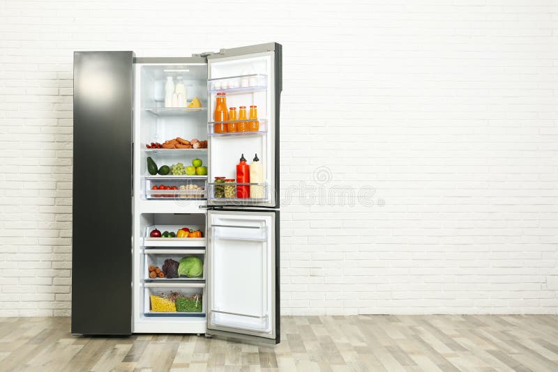 Open Refrigerator Filled with Food Near White Brick Wall, Space for