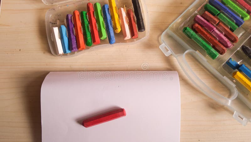 Open�sketchbook�and�a�red�crayon�on�top�is�next�to�rainbow�crayons on wooden table. Open�sketchbook�and�a�red�crayon�on�top�is�next�to�rainbow�crayons on wooden table.