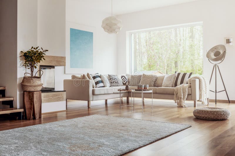 Open space, white living room interior with a big rug on dark, hardwood floor and a beige corner sofa with cushions concept