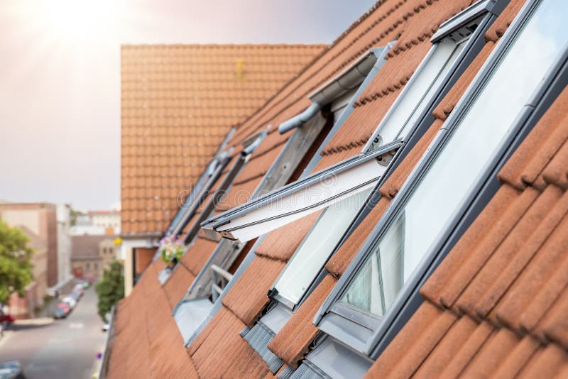 Open ventilation waterproof rooftop window exterior against sunny sky light. Velux style roof with red brick tiles