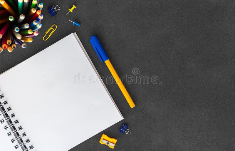 White blank spiral paper notebook with pen, cutter knife, eraser, paper clumps, paper clips, push pins on dark background stock image