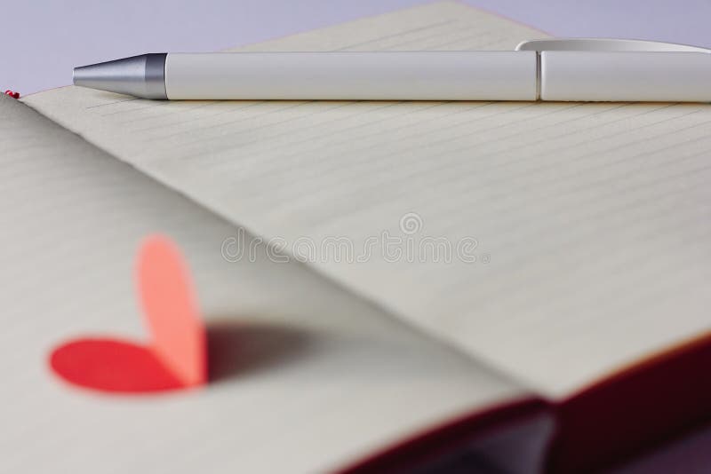 Opened blank notebook, pen and red paper heart