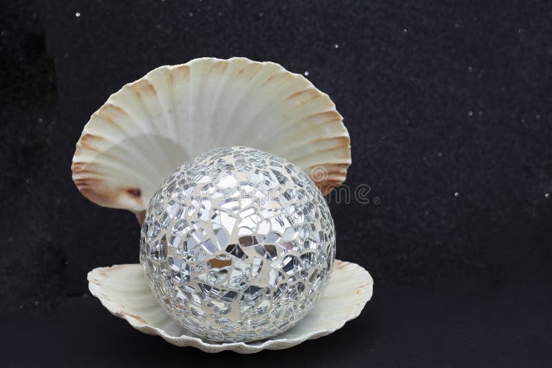 opened sea shell with a mirrors disco ball inside, isolated on black