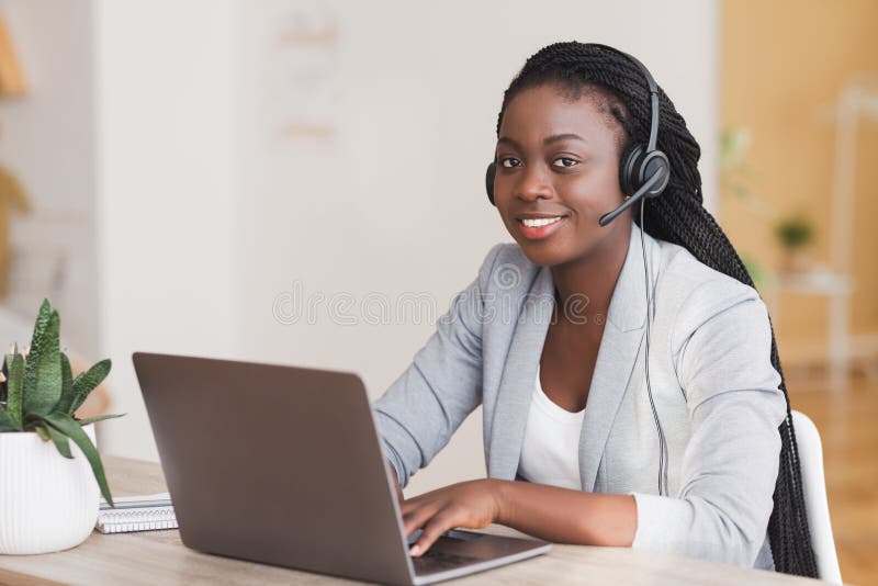 Operadora africana de atención al cliente que usa auriculares y trabaja en laptops