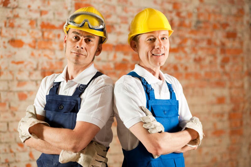 Operai di costruzione che si levano in piedi con le braccia piegate fotografia stock Operai di costruzione che si levano in piedi con le braccia piegate fotografia stock