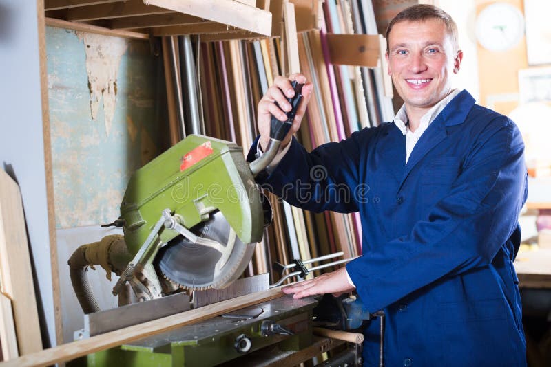 Operaio allegro che taglia le plance di legno facendo uso della sega circolare fotografia stock libera da diritti Operaio allegro che taglia le plance di legno facendo uso della sega circolare fotografia stock libera da diritti
