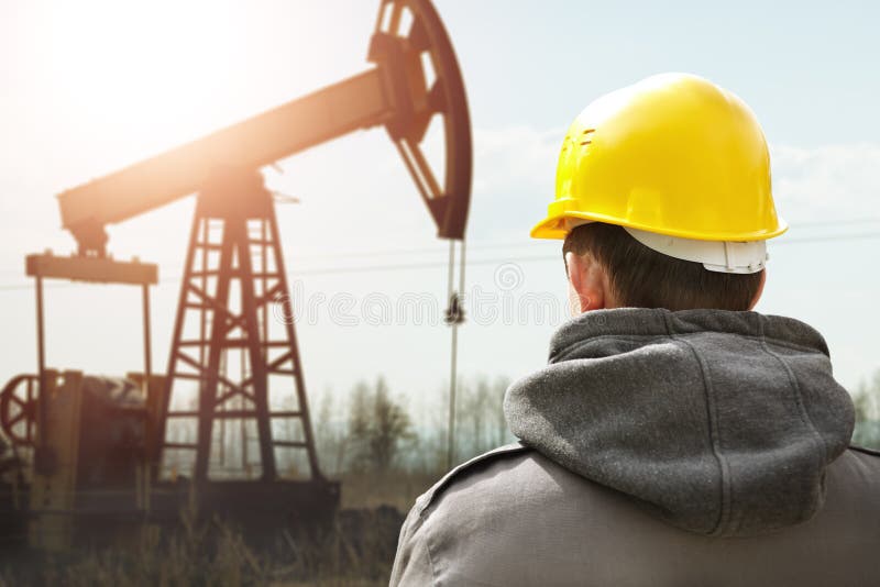 Oil worker in yellow helmet on of background the pump jack. Oil worker in yellow helmet on of background the pump jack