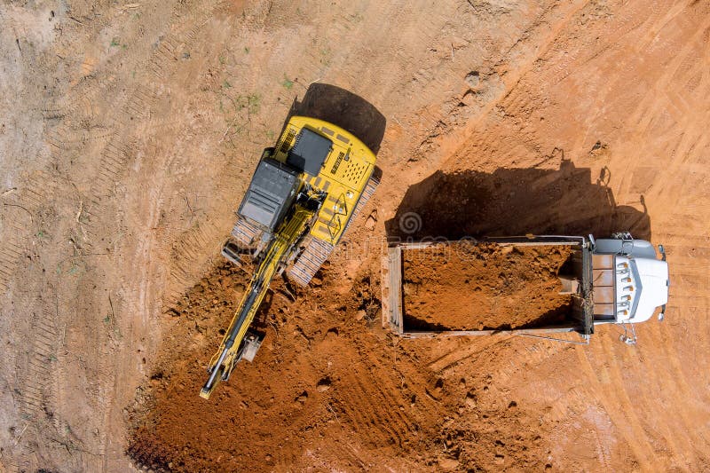 Excavator operator is carefully positioning scoop on soil is into dumper truck. Excavator operator is carefully positioning scoop on soil is into dumper truck