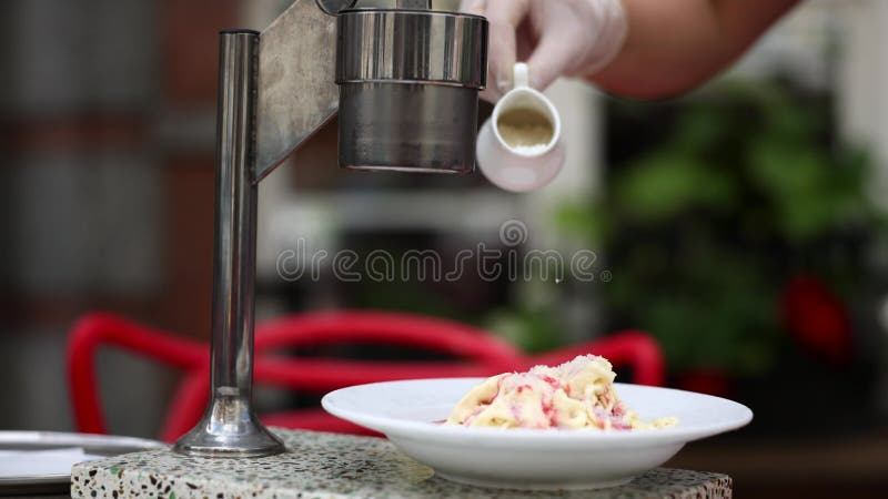 Operário no café, aspersão de nozes picadas para gelado acabado derramado por xarope de fruta