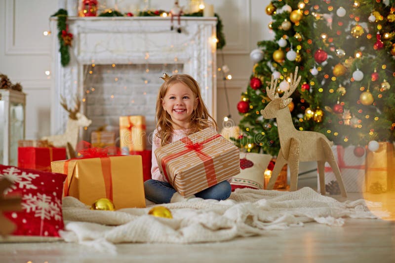 Opgewekt nieuwsgierig meisje die, het openen Kerstmisgiften glimlachen Prachtig verfraaid Kerstmisboom en huis met lichten en stock afbeeldingen Opgewekt nieuwsgierig meisje die, het openen Kerstmisgiften glimlachen Prachtig verfraaid Kerstmisboom en huis met lichten en stock afbeeldingen