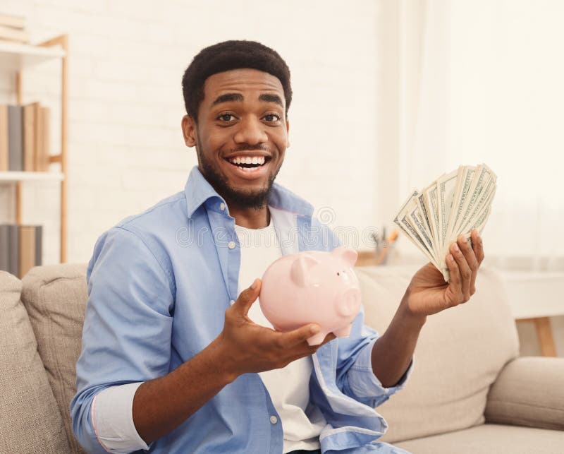 Opgewekte Afrikaans-Amerikaanse kerelholding piggybank en dollarrekeningen royalty-vrije stock foto's Opgewekte Afrikaans-Amerikaanse kerelholding piggybank en dollarrekeningen royalty-vrije stock foto's
