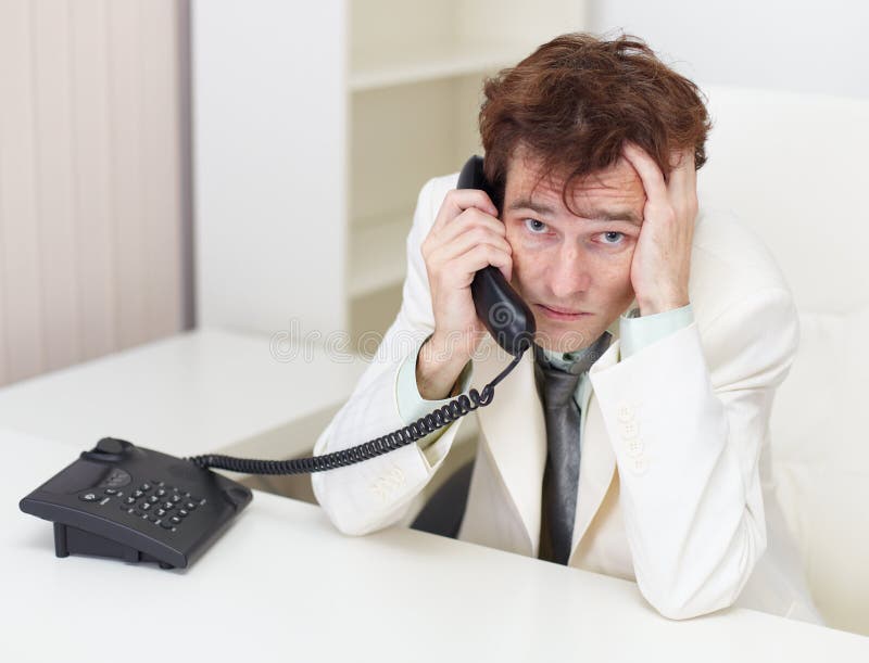 The person excited communicates by phone sitting at a table at office. The person excited communicates by phone sitting at a table at office