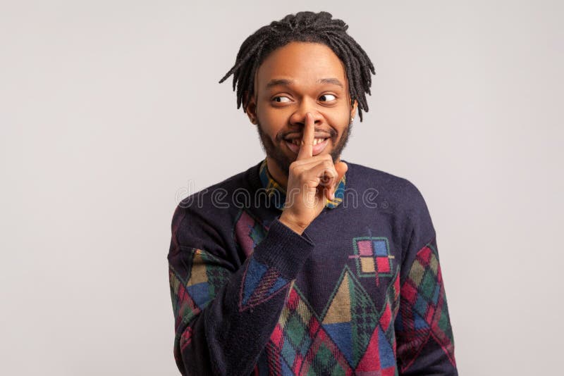 Excited african man with beard and dreadlocks showing shh gesture holding finger near mouth, cheerful happy with keeping secret. Indoor studio shot isolated on gray background. Excited african man with beard and dreadlocks showing shh gesture holding finger near mouth, cheerful happy with keeping secret. Indoor studio shot isolated on gray background