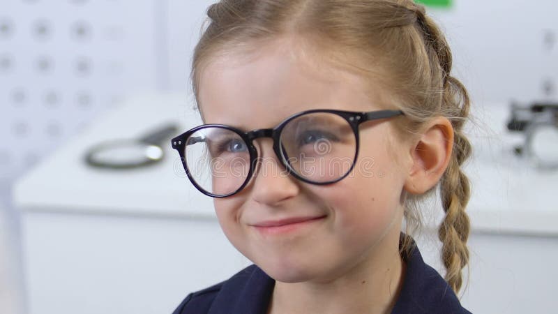 Ophthalmologist helping small girl to put on eyeglasses, corrective lenses