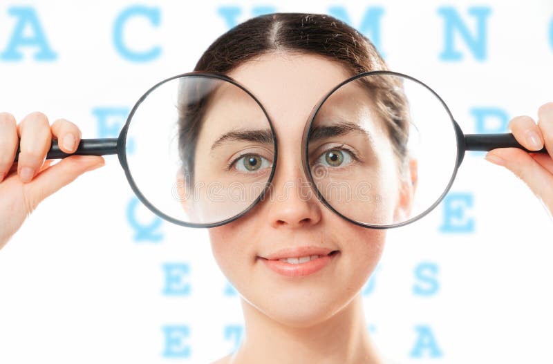 Ophthalmology. Portrait of a young smiling pretty woman holding magnifying glasses to her eyes. The alphabet is in the background. The concept of healthy eyes and an optical test.