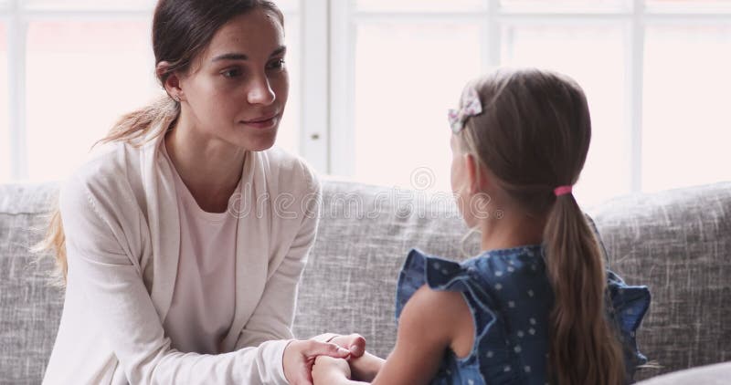 Opiekuńcza młoda mama trzymająca ręce rozmawiając z małą dziewczynką
