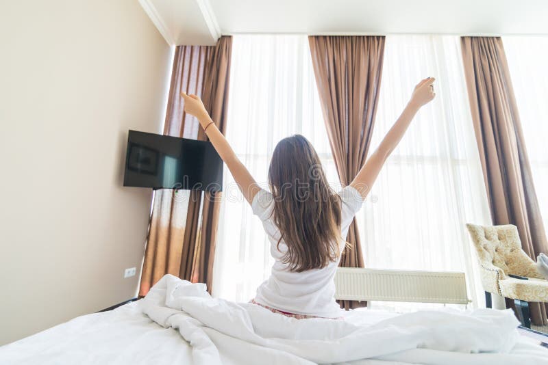 A opini?o traseira a jovem mulher que estica na cama ap?s acorda na manh? com luz solar fotografia de stock A opini?o traseira a jovem mulher que estica na cama ap?s acorda na manh? com luz solar fotografia de stock