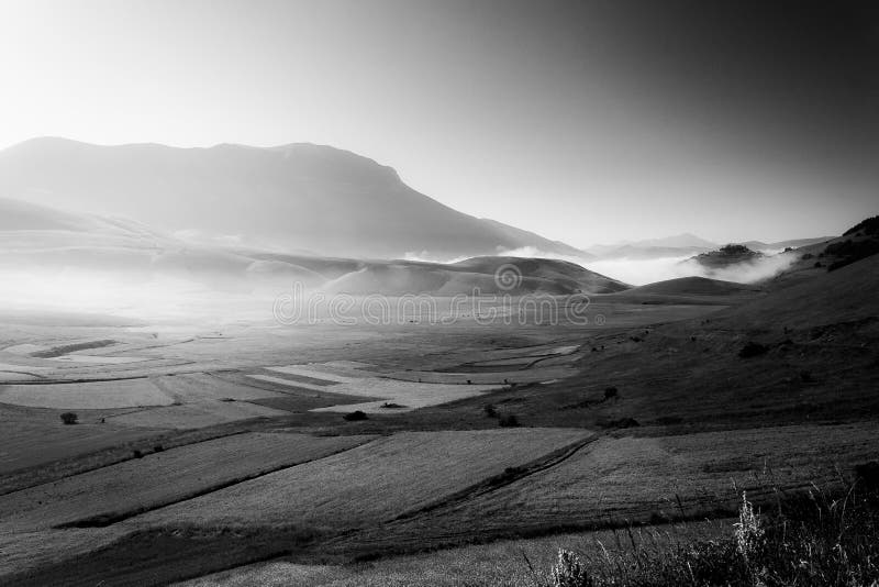 Opinião Castelluccio di Norcia Úmbria no alvorecer, com névoa, os prados grandes e o céu totalmente vazio imagens de stock Opinião Castelluccio di Norcia Úmbria no alvorecer, com névoa, os prados grandes e o céu totalmente vazio imagens de stock