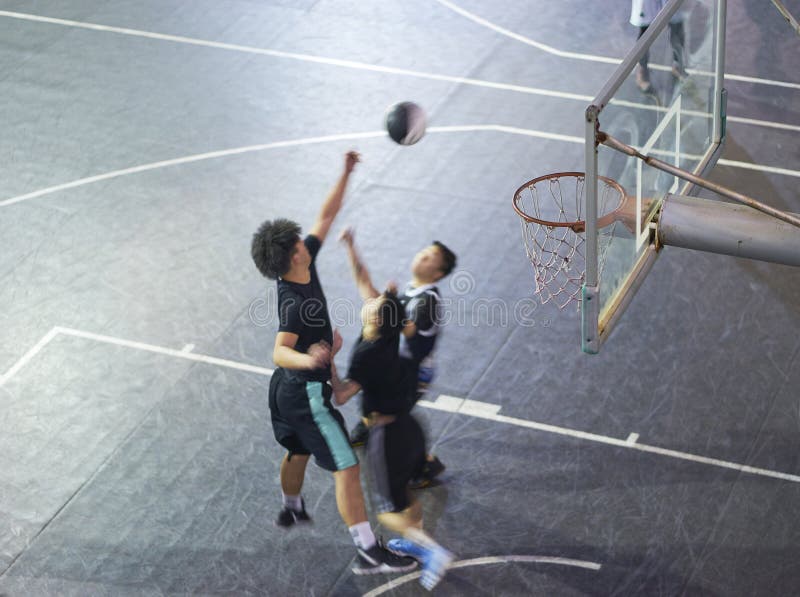 Opinião de ângulo alto os povos asiáticos novos que jogam o basquetebol exterior na noite imagens de stock Opinião de ângulo alto os povos asiáticos novos que jogam o basquetebol exterior na noite imagens de stock
