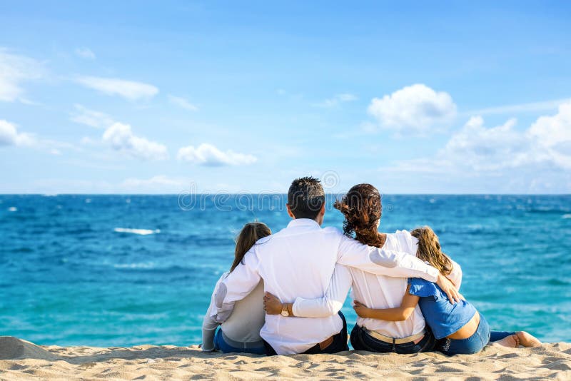Opinião traseira a família que senta-se junto na praia que olha o horizonte