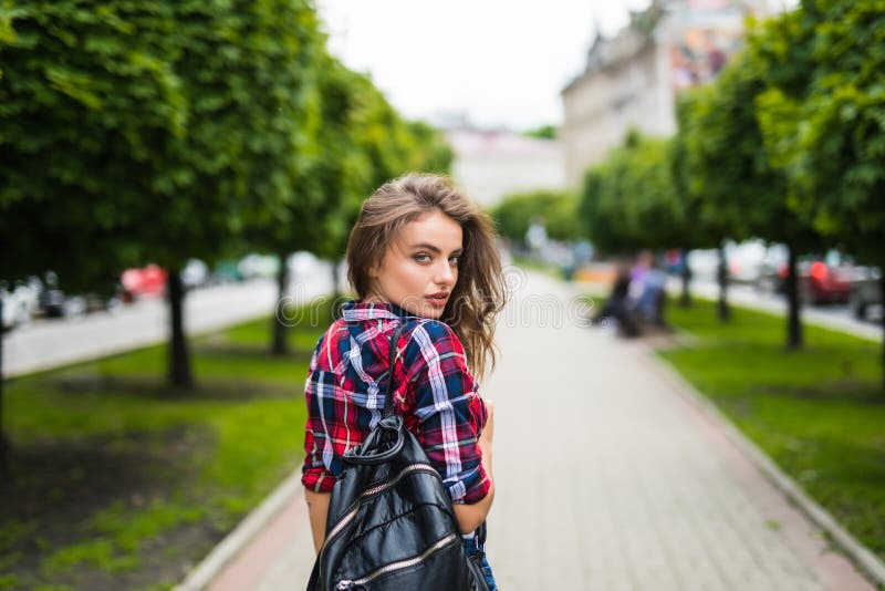 Opinião traseira a jovem mulher atrativa alegre com trouxa que anda no parque fotografia de stock Opinião traseira a jovem mulher atrativa alegre com trouxa que anda no parque fotografia de stock