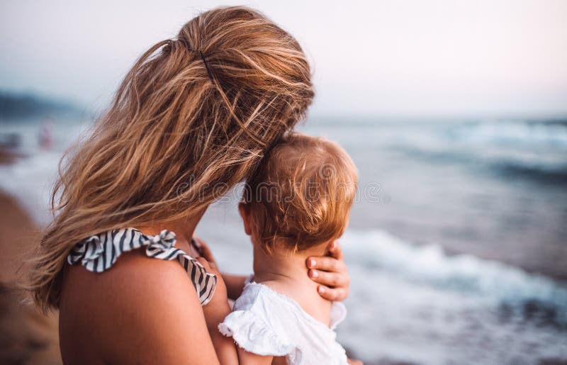 Opinião traseira a mãe nova com uma menina da criança na praia em férias de verão fotografia de stock Opinião traseira a mãe nova com uma menina da criança na praia em férias de verão fotografia de stock