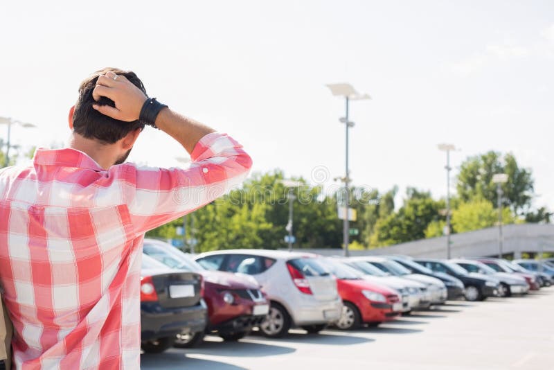 Rear view of man with hand behind head standing on city street against clear sky. Rear view of man with hand behind head standing on city street against clear sky