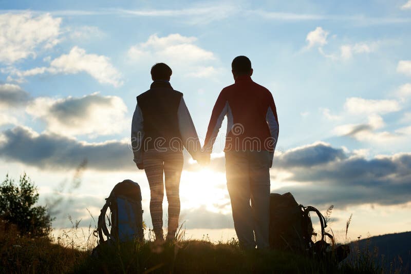 Opinião traseira os jovens que admiram o por do sol nas montanhas que guardam as mãos fotos de stock royalty free Opinião traseira os jovens que admiram o por do sol nas montanhas que guardam as mãos fotos de stock royalty free