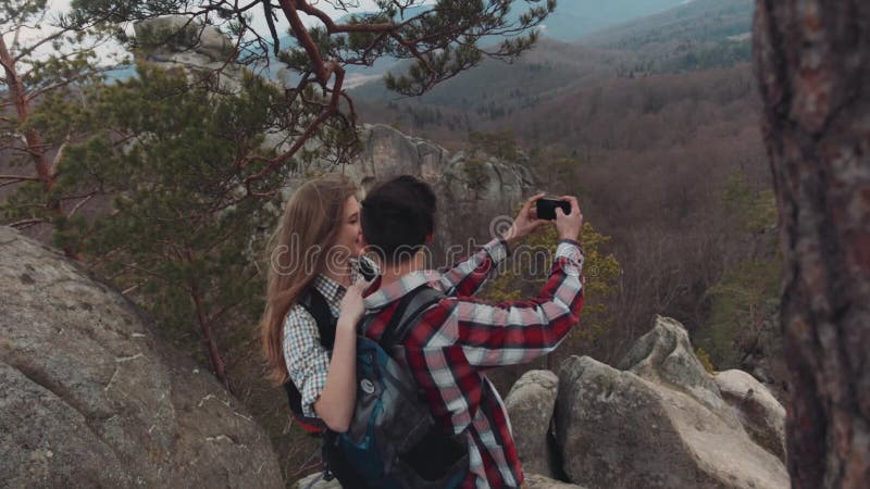 Opinión aérea una gente adorable joven que toma el selfie en el top de la montaña, de sonrisa, y de risa Paisaje magnífico