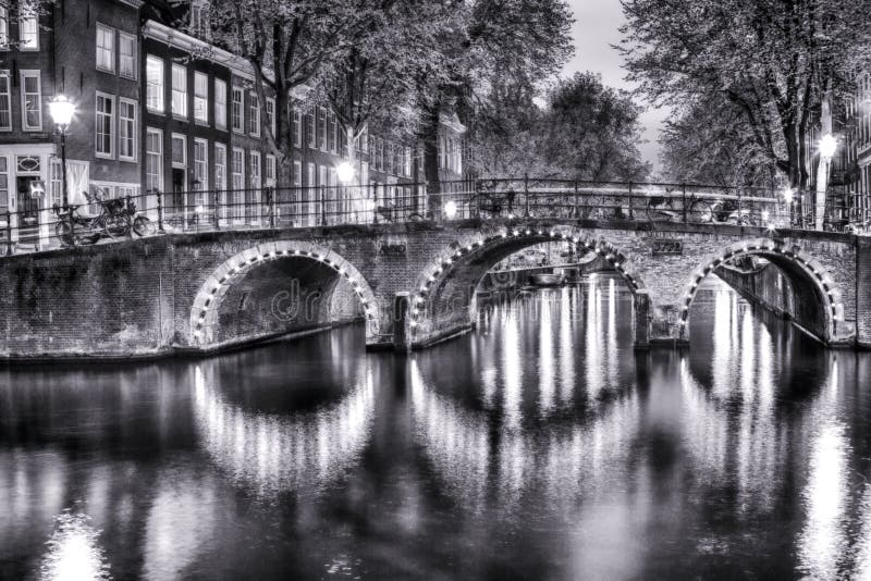 Opinión blanco y negro de la noche del paisaje urbano de Amterdam con uno de sus canales Con el puente iluminado y las casas hola