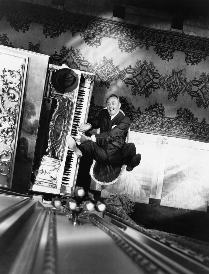 High angle view of a man reclining on a chair and playing a piano (All persons depicted are no longer living and no estate exists. Supplier grants that there will be no model release issues.). High angle view of a man reclining on a chair and playing a piano (All persons depicted are no longer living and no estate exists. Supplier grants that there will be no model release issues.)