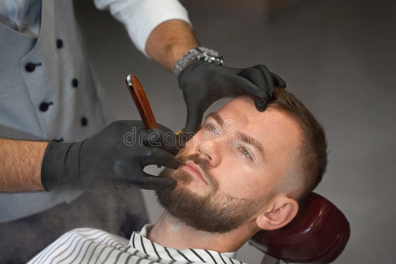 Opinión desde arriba del hombre en silla mientras que peluquero que afeita la barba foto de archivo libre de regalías Opinión desde arriba del hombre en silla mientras que peluquero que afeita la barba foto de archivo libre de regalías